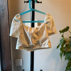 Vit croppad blus med broderade detaljer - Säljer en söt vit croppad blus med broderade hål och puffiga korta ärmar. Toppen har en fyrkantig ringning och är perfekt för varma dagar. Superfin att styla med jeans eller kjol!