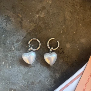 WOS ÖRHÄNGEN  - Säljer ett par silverfärgade örhängen med stora, hjärtformade pärlor som hänger ned. Perfekta för att ge en söt och trendig touch till din stil.