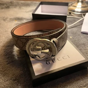 GG  bälte med silverfärgat spänne - Säljer ett klassiskt zara bälte med stort silverfärgat -spänne. Bältet har ett beige och brunt monogrammönster och är tillverkat i skinn med canvasöverdrag. Perfekt accessoar för att lyfta din outfit.