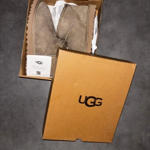 Uggs - Mysiga beige boots från UGG i mocka med låg skaft och mjukt foder. Skorna har en rund tå och platt sula, perfekt för kyliga dagar. Klassisk UGG-logga bak på hälen och dragflik för enkel påtagning.