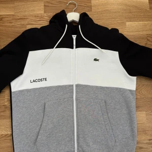 Lacoste kofta - Säljer en snygg hoodie från Lacoste i svart, vitt och grått. Koftan är storlek L.                          Priset kan diskuteras vid snabba affärer