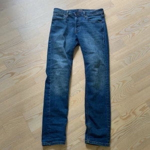 Blå jeansbyxor från Jack & Jones - Säljer ett par klassiska blå jeans från Jack & Jones, modell Slim Straight Tim. Jeansen har fem fickor, normal passform med raka ben och är tillverkade i denim. Perfekta för en stilren och enkel look.
