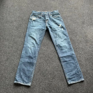 Blå jeansbyxor från Abercrombie & Fitch - Klassiska blå jeans från Abercrombie & Fitch med raka ben och slitna detaljer vid fickor och lår. Jeansen har fem fickor, gylf med dragkedja och knapp samt läderpatch bak i midjan.