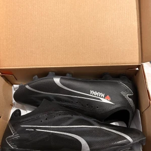 Svarta fotbollsskor med silverdetaljer - Säljer ett par svarta Nike fotbollsskor med silverfärgade detaljer och texten 'MAMMA❤️' med ett hjärta på sidan. Skorna har snörningsfri design och dobbar för spel på gräs/konstgräs. Perfekta för dig som vill sticka ut på planen.