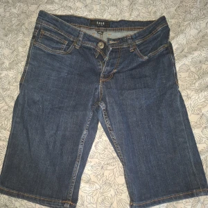 Jeansshorts från SMOG - Säljer ett par klassiska blå jeansshorts från SMOG med normal passform. Shortsen har fem fickor, knapp och dragkedja framtill samt snygga kontrastsömmar. Perfekta för varma dagar och enkel att matcha med t-shirt eller skjorta.