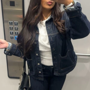 Mörkblå jeansjacka från ZARA - Säljer en klassisk mörkblå jeansjacka från ZARA i storlek XS. Jackan har stora framfickor, knappar framtill och kontrastsömmar. Perfekt att styla med både t-shirt och hoodie. Snygg och tidlös modell!