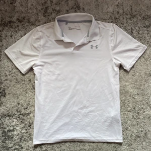 Vit träningspiké från Under Armour - Vit pikétröja från Under Armour. Tröjan är tillverkad i ett syntetmaterial med HeatGear-teknologi som håller dig sval. Perfekt för sportiga aktiviteter.