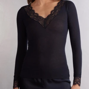 Svart långärmad topp med spetsdetaljer - Svart långärmad topp med  v-ringning och fina spetsdetaljer längs halsringningen och vid ärmsluten. Tunn och stretchig modell som sitter snyggt på kroppen. Perfekt att styla till olika looks. I storlek M