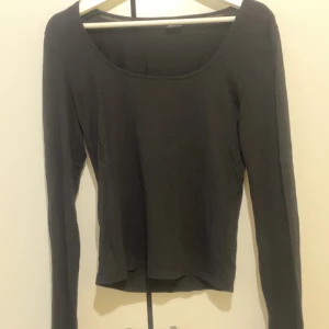 Svart långärmad topp från Gina Tricot - En enkel och stilren svart långärmad topp från Gina Tricot med rundad, något djupare halsringning. Perfekt att matcha med jeans eller kjol för en clean look.