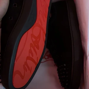 Svarta sneakers med nitar från Christian Louboutin - Säljer ett par svarta sneakers från Christian Louboutin med klassisk röd sula och svarta nitar på tån. Skorna är i mocka och har snörning. Perfekta för dig som vill sticka ut med exklusiva detaljer och ikonisk design. skorna har använt 4 gånger prisen kan diskutera snabb affär