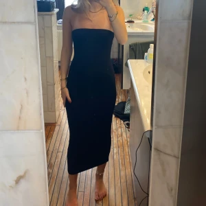 Svart axelbandslös långklänning - Säljer en svart axelbandslös långklänning med tight passform. Klänningen har en stilren och minimalistisk design med slits baktill för extra rörelsefrihet. Perfekt för dig som gillar en enkel men elegant look.