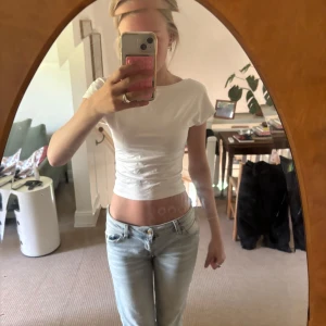 Vit croppad topp med öppen rygg - Säljer en vit croppad topp med tight passform och korta ärmar. Toppen har en snygg öppen rygg som ger en unik look. Perfekt till jeans eller kjol för en trendig stil.