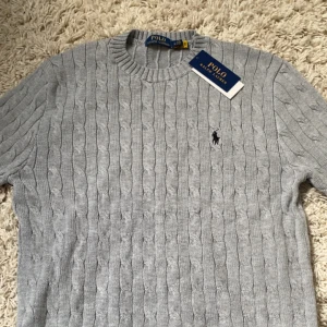 Kabelstickad tröja från Polo Ralph Lauren - Säljer en ljusgrå kabelstickad tröja från Polo Ralph Lauren. Helt ny! Prövad en gång. Perfekt för en stilren och snygg look. Storlek M men passar också L! Priset kan diskuteras vid snabb affär! 