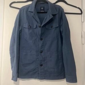 Blå overshirt från Lindbergh - Snygg blå overshirt från Lindbergh med klassisk krage och knäppning framtill. Jackan har två bröstfickor med knappar och två sidofickor. Perfekt lager-på-lager-plagg med stilren look.