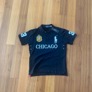 Polo Ralph Lauren “Chicago” Piké - Storlek: S Skick: Ny med tags (helt oanvänd) Färg: Svart Ikonisk Ralph Lauren pikétröja med stor logga, broderade detaljer och “CHICAGO”-tryck framtill. Ett riktigt statement-plagg som sticker ut! Perfekt för både vardag och mer uppklädda tillfällen. 📦 Levereras med originaltagg kvar. 💬 Pris kan diskuteras vid snabb affär!