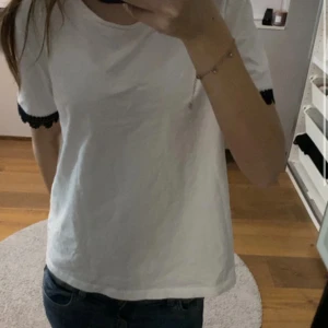 vit t-shirt med svarta spetsdetaljer - jag säljer en t-shirt med korta ärmar och svarta spetsdetaljer vid slutet av ärmarna. har inte kommit till andvädning, den är väldigt ny 💕