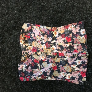 Blommig tubtopp med knappar - Säljer en blommig tubtopp i mörkblått med röda, gula och vita blommor. Toppen har dekorativa knappar framtill och är perfekt för sommaren. Snygg och trendig modell som passar till både jeans och kjol.