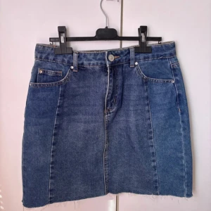 Blå jeanskjol  - Säljer en klassisk blå jeanskjol med fem fickor och rå, ofållad nederkant. Kjolen har normal passform och bälteshällor i midjan. Kjolen är helt ny men saknar prislapp.