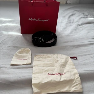 Svart skärp från Salvatore Ferragamo - Stilrent svart skärp från Salvatore Ferragamo med ikoniskt dubbel-Gancini spänne i svart metall. Skärpet är tillverkat i slätt skinn och levereras med originalpåse och presentpåse.