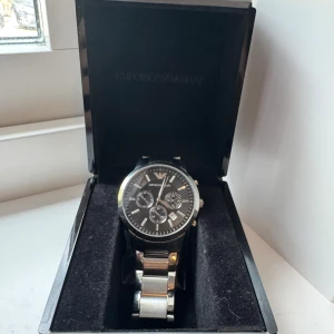 Emporio armani klocka - Stilren herrklocka från Emporio Armani med svart urtavla, silverfärgade detaljer och länkarmband i metall. Klockan levereras i originalask och extra länkar medföljer. Perfekt accessoar för dig som gillar klassisk design. Skick-8/10.