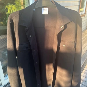 Svart overshirt från Selected Homme - Säljer en svart overshirt från Selected Homme med klassisk krage och tryckknappar framtill. Skjortan har två bröstfickor med lock och lång ärm. Knappt använd! 