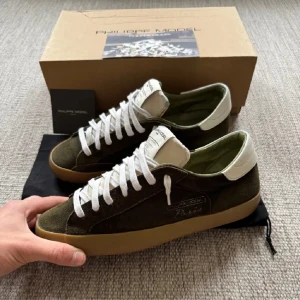 Olivgröna sneakers från Philippe Model - Säljer ett par olivgröna Philippe Model sneakers med vit hälkappa och vita snören. Skorna har en klassisk låg profil, rund tå och platt gummisula. Ovandelen är i mocka och detaljerna är stilrena. Perfekta för dig som gillar en clean och tidlös look. Passar 42/43. Går ner i pris vid snabb affär 