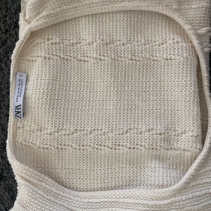 Vit stickad linnetopp med volang från Zara - Säljer en vit stickad linnetopp från Zara med flätstickat mönster och volangdetaljer längs sidorna. Toppen är ärmlös och har en mjuk, ribbad känsla. Perfekt för vår och sommar! Har inte använts lite stor köptes för 300 kr säljer för 250 priset kan diskuteras 