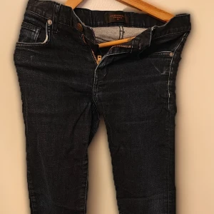 Mörkblå jeans från J.Lindeberg - Snygga mörkblå jeans från J.Lindeberg med klassisk femficksdesign och guldfärgad dragkedja. Jeansen har normal passform och raka ben, perfekta till vardags. Märkespatch i svart läder baktill i midjan och guldlogo på framsidan.  