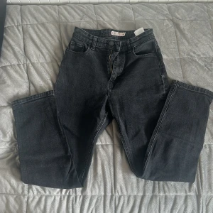 Svarta raka jeans - Säljer ett par svarta jeans med rak passform och klassisk femficksdesign. Byxorna har hög midja och stängs med dragkedja och knapp. Perfekta till vardags för en stilren look.