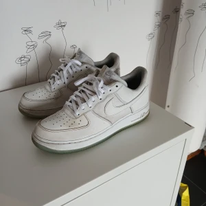 Vita Nike Air Force 1 sneakers - Klassiska vita Nike Air Force 1 sneakers med lågt skaft och snörning. Skorna har en rund tå, platt sula och är tillverkade i skinn med diskreta grå detaljer. Perfekta för en stilren och sportig look. Storlek 43 passar även 42. Är lite smutsiga men kan nog tvättas bort, annars i bra skick. 