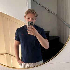 Mörkblå t-shirt från Polo Ralph Lauren - Säljer en mörkblå t-shirt från Polo Ralph Lauren med klassisk röd broderad logga på bröstet. T-shirten är i mjuk bomull (Pima Soft Touch) och har normal passform med korta ärmar. Perfekt basic-plagg med stilren look. Några små fläckar som knappt märks av vid användning 