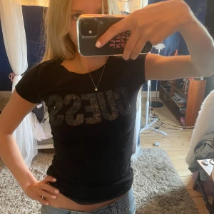Svart t-shirt från Guess med paljetter - Säljer en jättesnygg svart t-shirt från Guess med glittriga paljetter på bröstet som bildar loggan. T-shirten har en tight passform och är tillverkad i mjuk bomull. Säljer då den tyvärr ej kommer till andväning! 💞