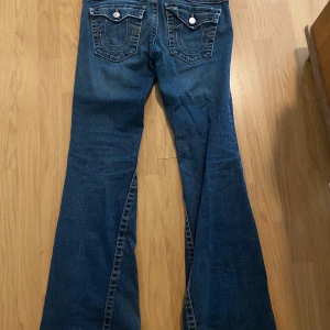 Blå bootcut jeans med fickdetaljer - Säljer ett par blå bootcut jeans från true religon. Storlek 30w är 174 och går ner hela vägen o lite till, har vanligtvis 38 i byxor för referens. Finns lite slitningar ner till!… Köpt på vintage&friends!