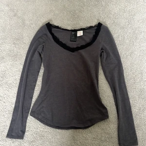 Mörkgrå långärmad topp med spets från H&M - Säljer en mörkgrå långärmad topp från H&M i storlek XS. Toppen har en v-ringad hals med svart spetsdetalj runt urringningen. Mjuk och stretchig bomullsblandning, perfekt till många olika outfits.💕 
