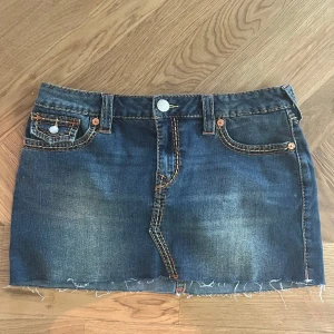 Jeanskjol från True Religion - Säljer en blå jeanskjol från True Religion med rå kant nertill och klassiska kontrastsömmar. Kjolen har fem fickor och detaljerade bakfickor med lock och knapp. Perfekt för dig som gillar street och denim.  Helt nytt skick, aldrig använd! 💕I kjolen står det storlek: 29
