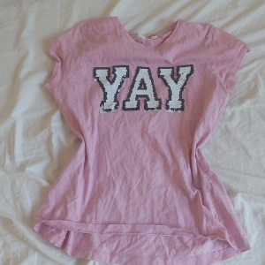 Y2k T-shirt med paljetttext - Rosa t-shirt med stort YAY-tryck i paljetter på bröstet. T-shirten har rund halsringning och korta ärmar. Perfekt för dig som vill sticka ut lite extra med glittriga detaljer. Perfekt om du vill va y2k på sommaren🫶🫶