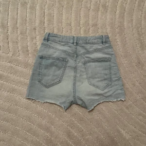 Ljusblå jeansshorts från Lindex - Ljusblå jeansshorts från Lindex med råa kanter och klassisk femficksdesign. Shortsen har bälteshällor och knappstängning framtill. Perfekta för varma dagar och enkel att matcha med olika toppar. Kolla min profil för fler kläder!