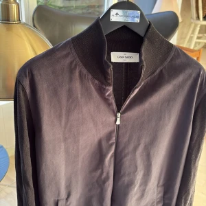 Gran Sasso - Knappt använd Stilren svart jacka från Gran Sasso med dragkedja och hög krage. Jackan är tillverkad och köpt i italien, riktigt högt kvalite! Jackan är i alcantara. Perfekt för dig som gillar lyx och något som är perfekt och riktigt snyggt i sommar som är lätt att slänga på! Passar s och xs!