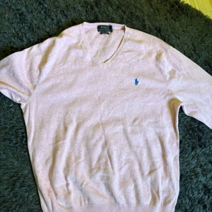 Ljusrosa v-ringad tröja från Polo Ralph Lauren - Säljer en ljusrosa v-ringad tröja från Polo Ralph Lauren i mjuk pima bomull. Tröjan har lång ärm och en broderad blå logga på bröstet. Perfekt för dig som gillar klassisk och stilren design. Storlek M i väldigt bra skick inga defekter 