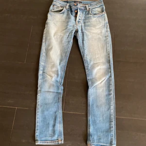 Ljusblå jeans från Nudie Jeans - Säljer ett par klassiska ljusblå jeans från Nudie Jeans med orangea sömmar och snygga detaljer på bakfickan. Jeansen har normal passform och raka ben, perfekta till vardags. Storlek W31 L32.