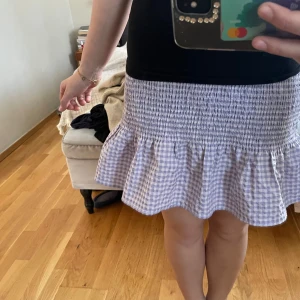Lila rutig kjol från H&M - Säljer en söt lila rutig kjol från H&M:s Divided-kollektion. Kjolen har en volangdetalj längst ner och en elastisk midja för en bekväm passform. Perfekt för en avslappnad och stilren look.