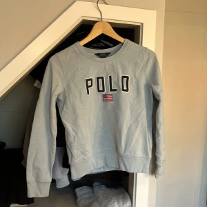Ljusblå sweatshirt från Polo Ralph Lauren - Säljer en ljusblå sweatshirt från Polo Ralph Lauren med texten 'POLO' och en liten amerikansk flagga på framsidan. Tröjan har krympt lite i tvätten men är fortfarande i bra skick, storlek 160 men funkar för dom som har mindre storlek oxå💞 hoppas nån vill köpa!