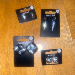 Snygga örhängen från Montini - Upptäck tre olika par örhängen från Montini. Ett par med stora, vridna silverknutar, ett par med glänsande silverkulor och ett par med glittrande droppar. Perfekta accessoarer för att lyfta din stil, inte använda 