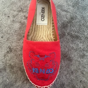 Röda espadrillos från Kenzo - Snygga röda espadrillos från Kenzo med ett broderat tigerhuvud och logotyp i blått framtill. Skorna har en klassisk espadrillosula i naturmaterial och är perfekta för en avslappnad stil.