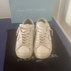 Vita sneakers från Philippe Model - Snygga vita sneakers från Philippe Model med klassisk design och snörning. Skorna har en rund tå och är perfekta för en stilren look. De kommer med originalförpackning och påse. Skorna passar även 42.Pris kan diskuteras.