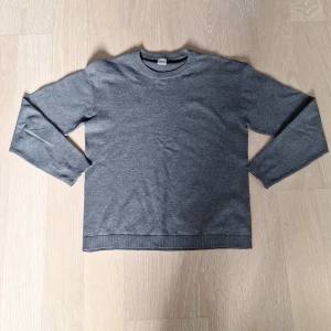 Grå långärmad tröja från Lindex - En enkel och stilren grå långärmad tröja från Lindex. Tröjan har rund halsringning och är tillverkad i mjukt och streck material som passar perfekt till vardags. Klassisk passform och diskret design gör den lätt att matcha med andra plagg.