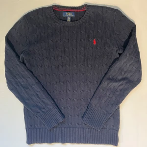 Stickad tröja från Ralph Lauren - Mörkblå kabelstickad tröja ifrån Ralph Lauren. Storleken 14/16 år vilket passar de som är runt 170 (xs). Skick på den är 9/10 knappt använd. Självklart äkta. Bara höra av sig vid någon fundering. Priset är inte hugget i sten, kom gärna med bud!