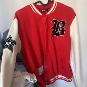 Röd och vit collegejacka från FB Sister - Säljer en röd och vit collegejacka från FB Sister med broderade bokstäver och stjärndetalj på ärmen. Jackan har tryckknappar framtill