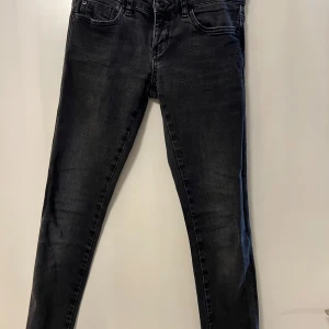 Svarta skinny jeans-Replay  - Säljer ett par mörkgråa skinny jeans med klassisk femficksdesign och knappgylf. Jeansen har en smal passform och är tillverkade i stretchigt denim för extra komfort.