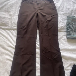 Bruna kostymbyxor med bootcut - Säljer ett par bruna kostymbyxor från Gina tricot med bootcut-passform. Byxorna har låg midja.